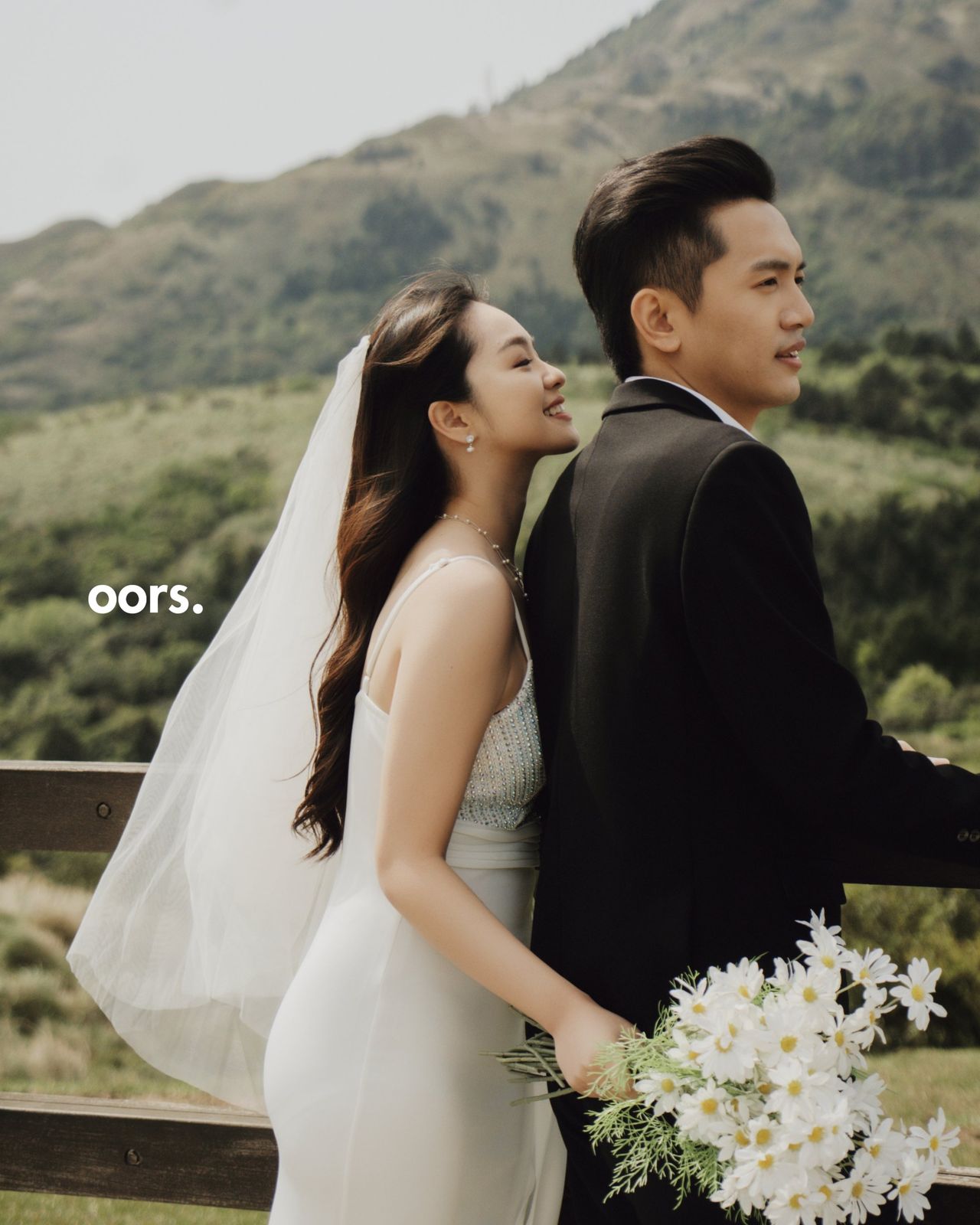 The couple embracing against a green mountain, a veil in the wind