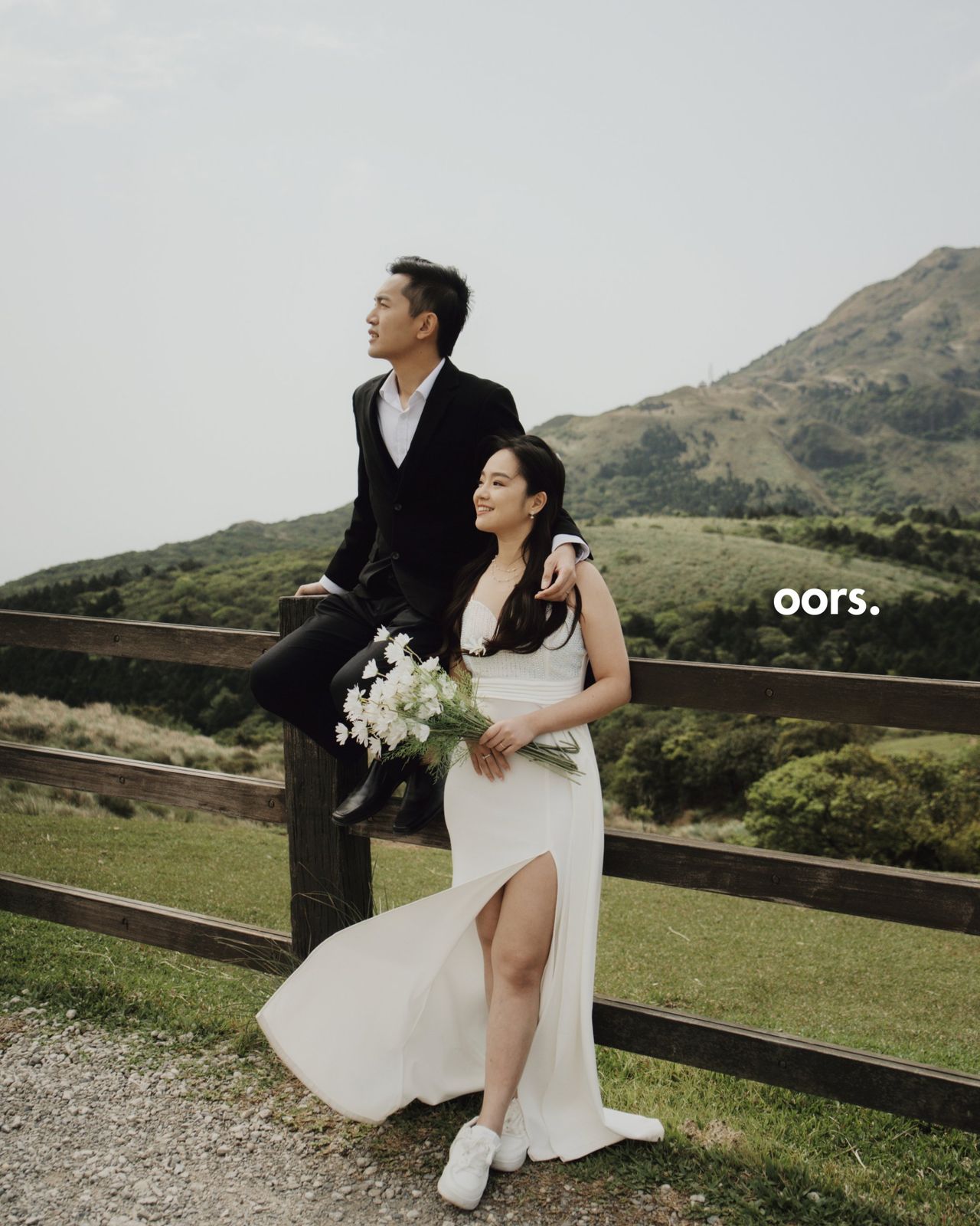 The couple resting against a wooden fence in the hills