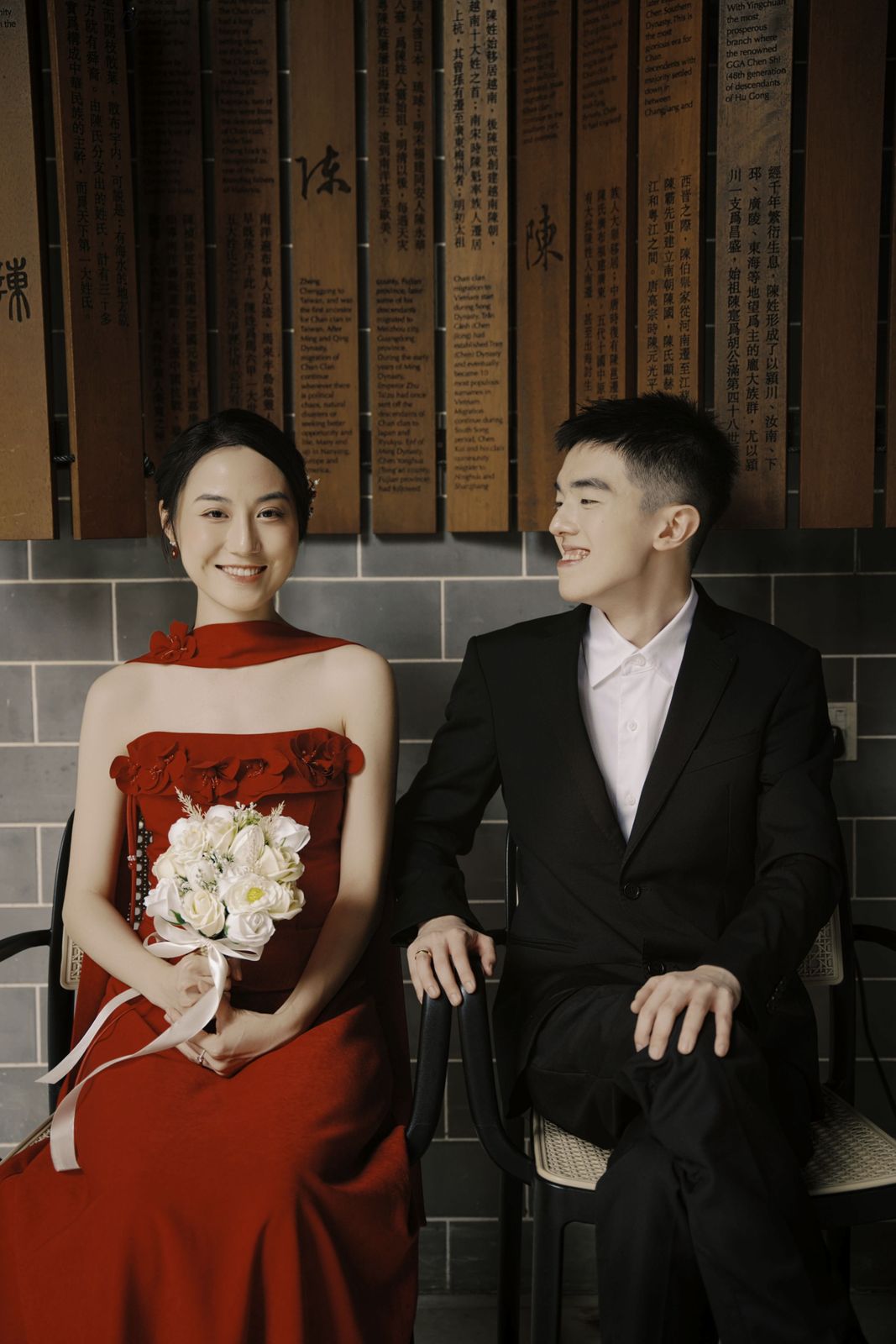 The couple seated against a wall of clan name plaques, the bride holding a bouquet