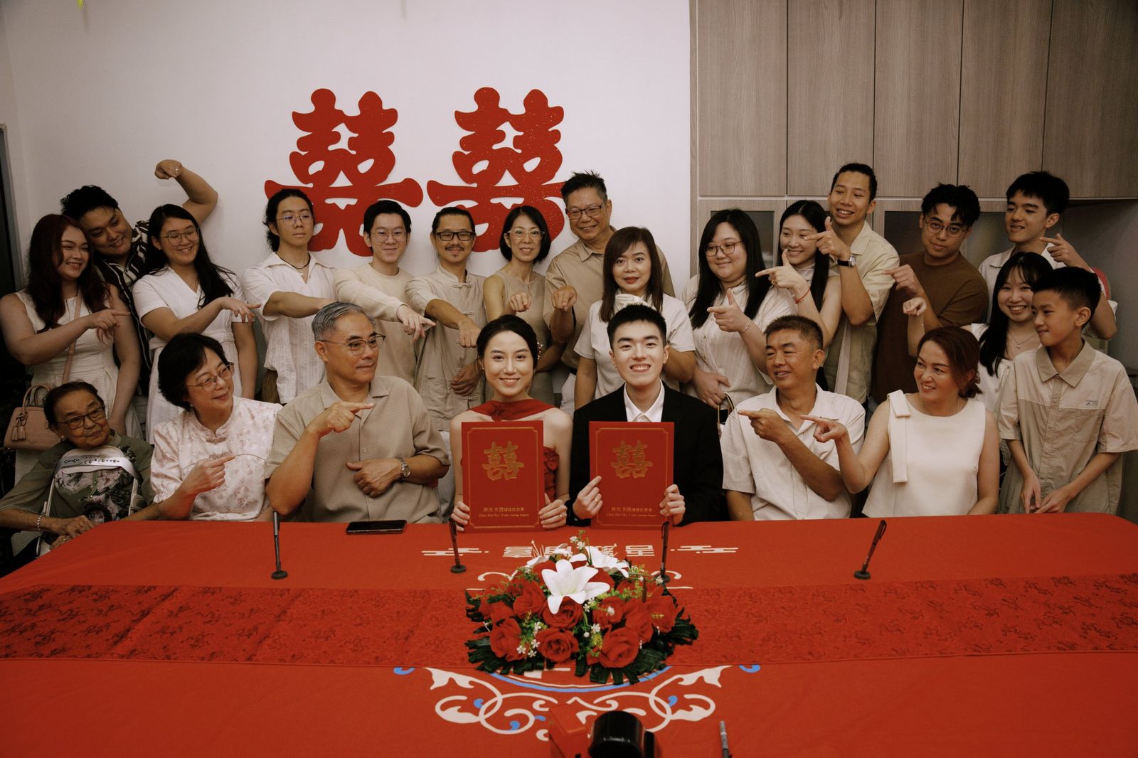 The couple holding their certificates, surrounded by family and friends