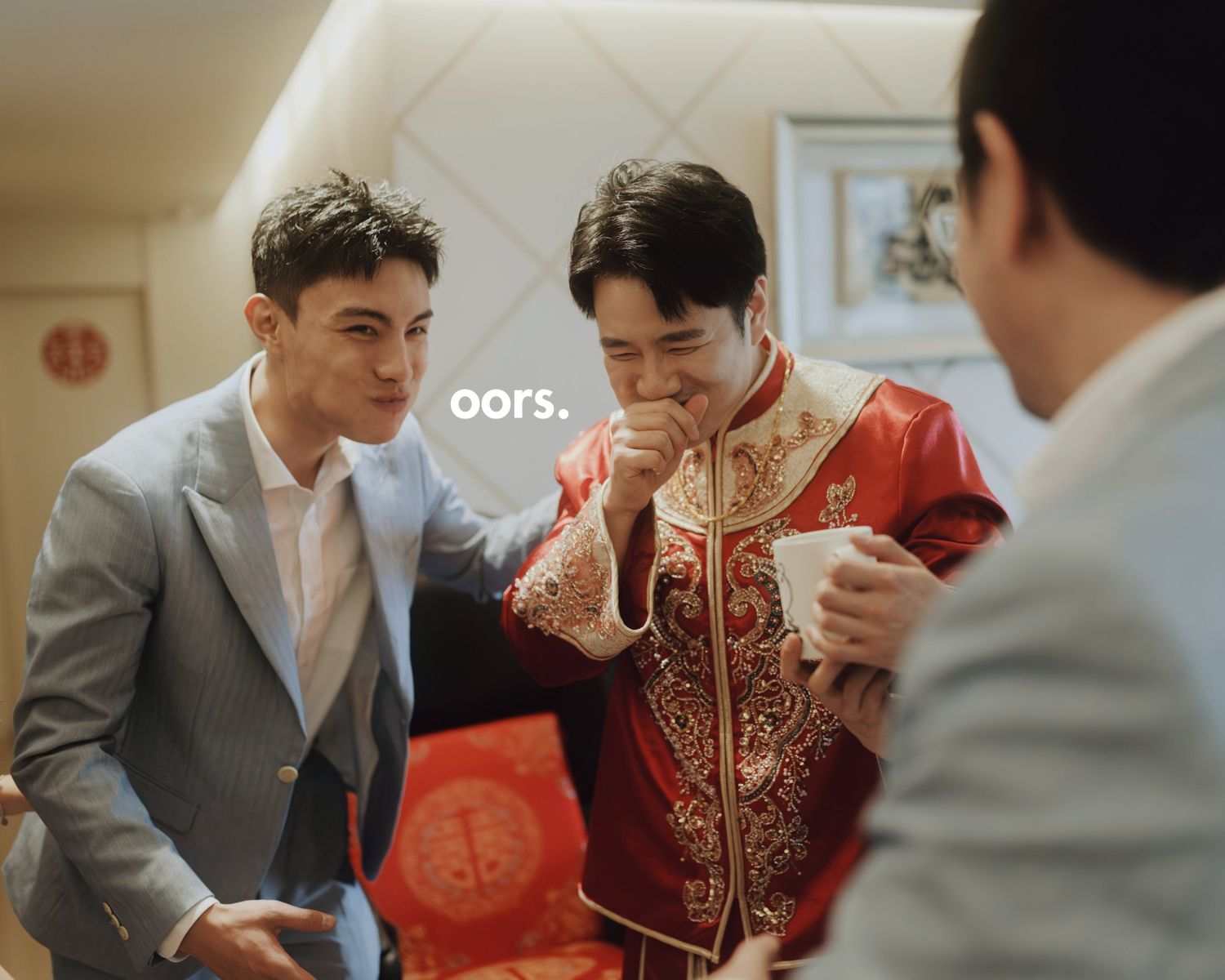 The groom laughing in a red wedding jacket