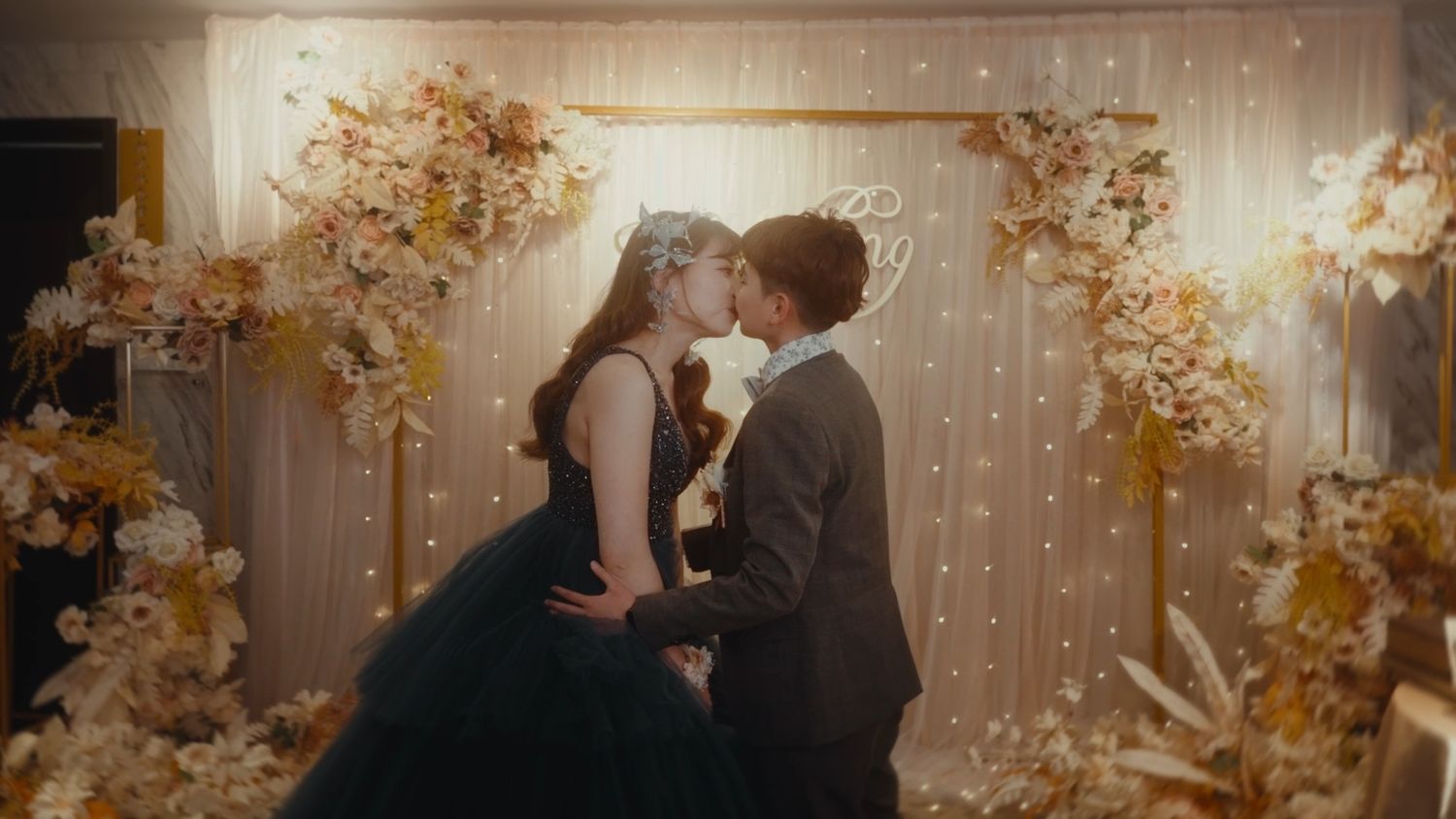 The couple sharing a kiss before a wall of fairy lights